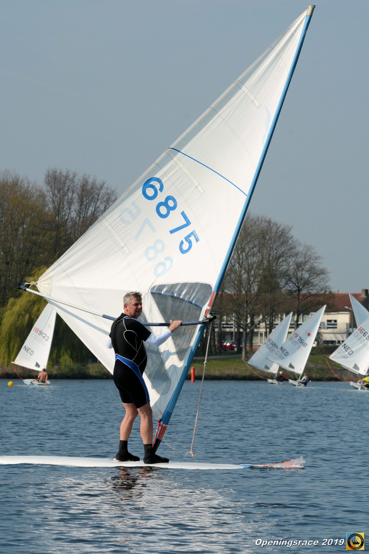 Een windsurfer vaart tussen zeilboten tijdens de Openingsrace ZVO 2019.