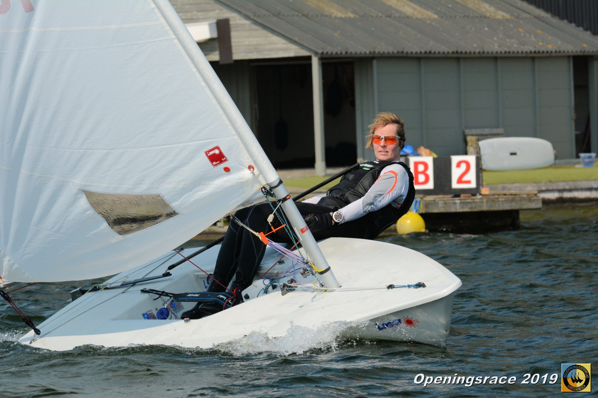 Een zeiler hangt uit in een Laser zwaardboot bij het clubhuis tijdens de Openingsrace ZVO 2019.