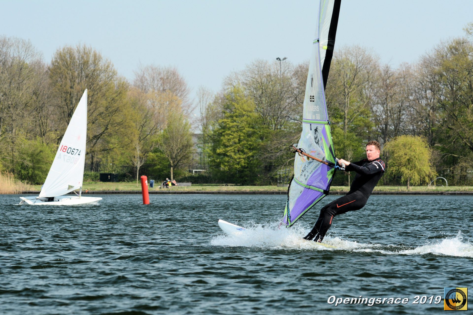 Een windsurfer en een zwaardboot varen bij een rode boei tijdens de Openingsrace ZVO 2019.
