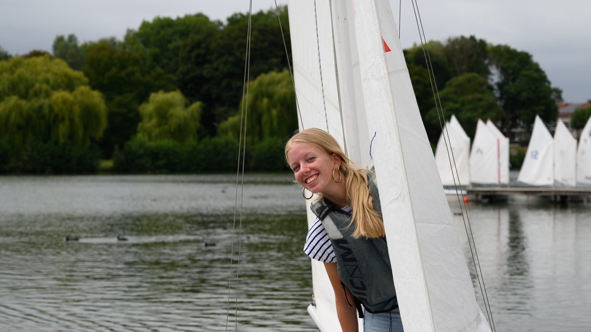 Een zeiler kijkt lachend om het zeil heen op de Oosterplas.