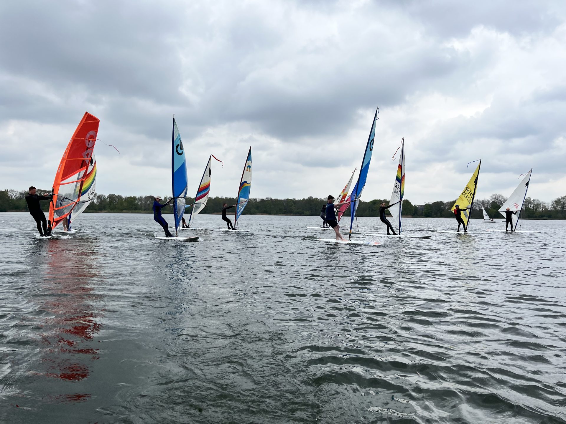 Windsurfers varen op de Oosterplas onder bewolkte lucht.