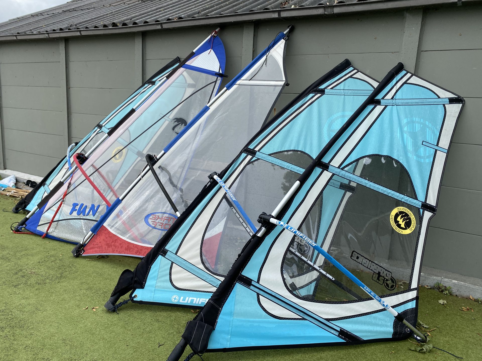 Rij blauwe en roze surfzeilen staat klaar tegen de loods bij ZVO.