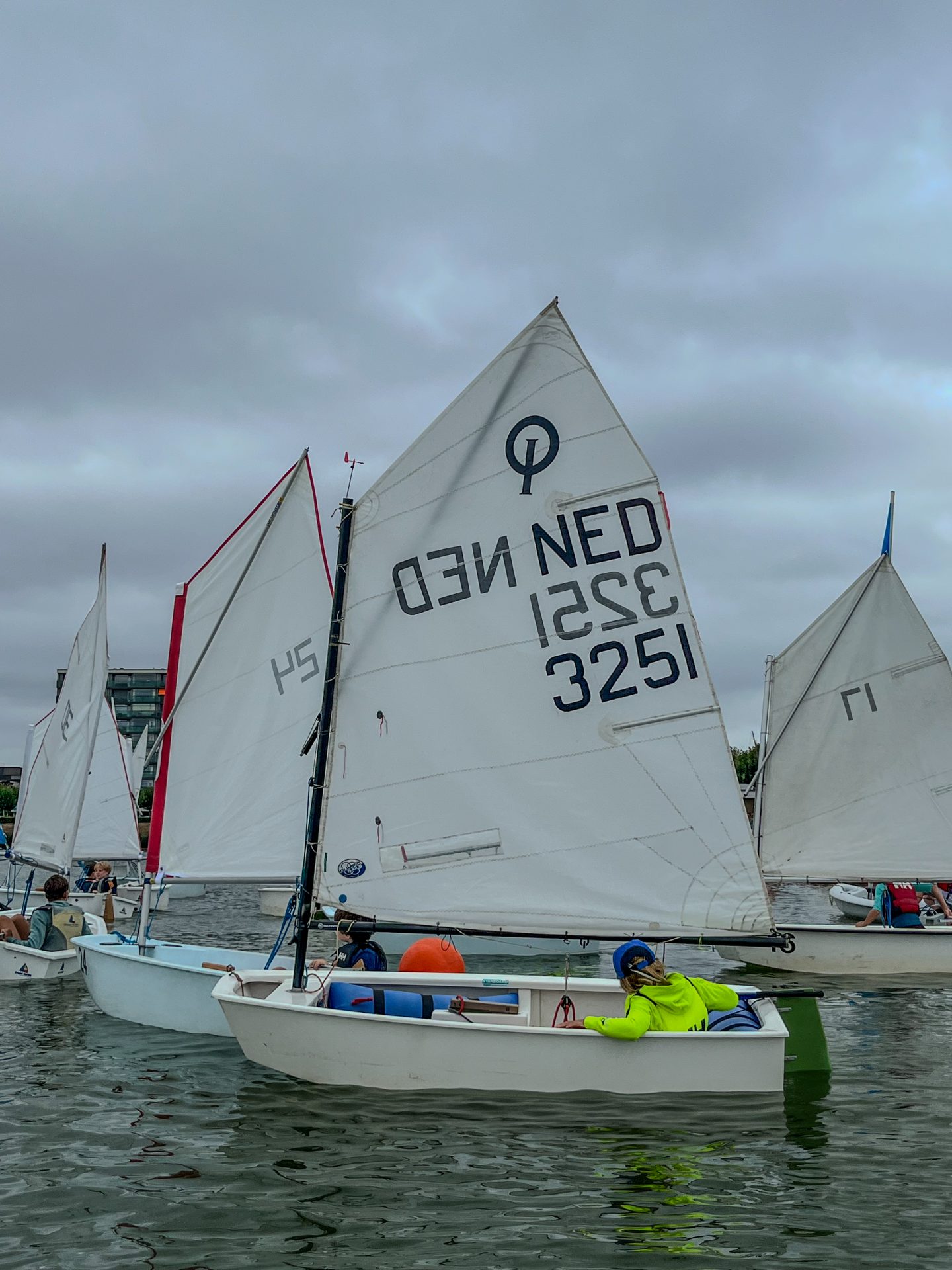 Een groep deelnemers is bij Optimist zeilboten tijdens CWO les.