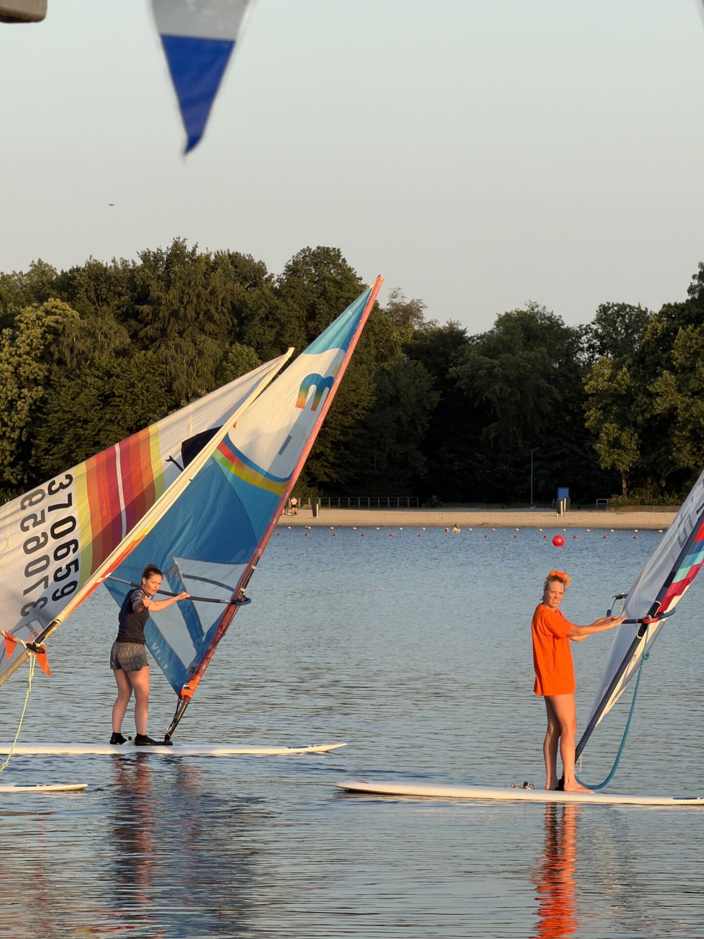 Twee windsurfers staan met zeilen op surfplanken op de Oosterplas tijdens Midzomernacht 2026.