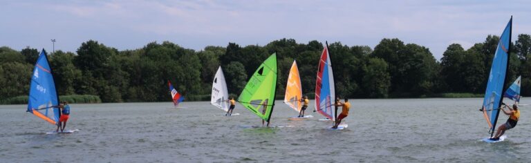 Meerdere windsurfers varen met gekleurde zeilen op de Oosterplas.