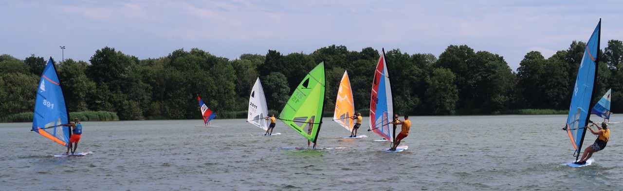 Meerdere windsurfers varen met gekleurde zeilen op de Oosterplas.