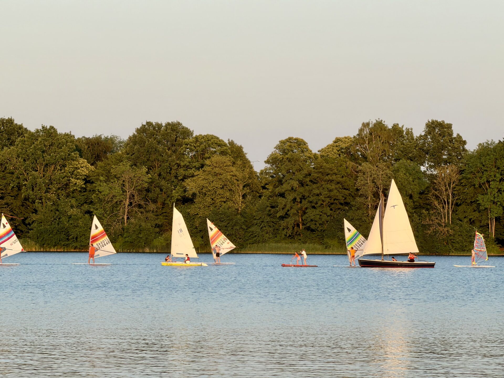 Zeilboten en windsurfers varen bij avondlicht op de Oosterplas.