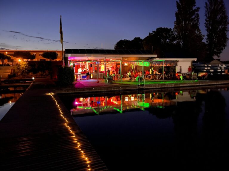 Het clubhuis is verlicht en weerspiegelt in het water tijdens Midzomernacht 2026.