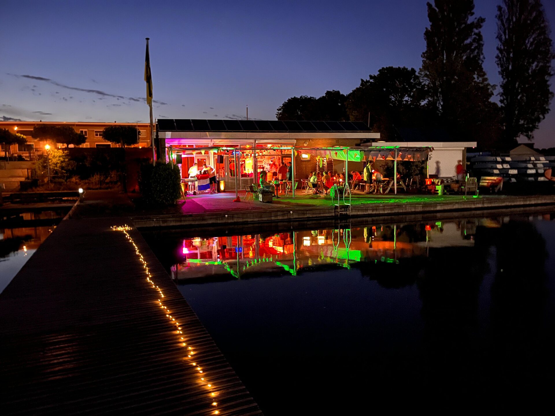 Het clubhuis is verlicht en weerspiegelt in het water tijdens Midzomernacht 2026.