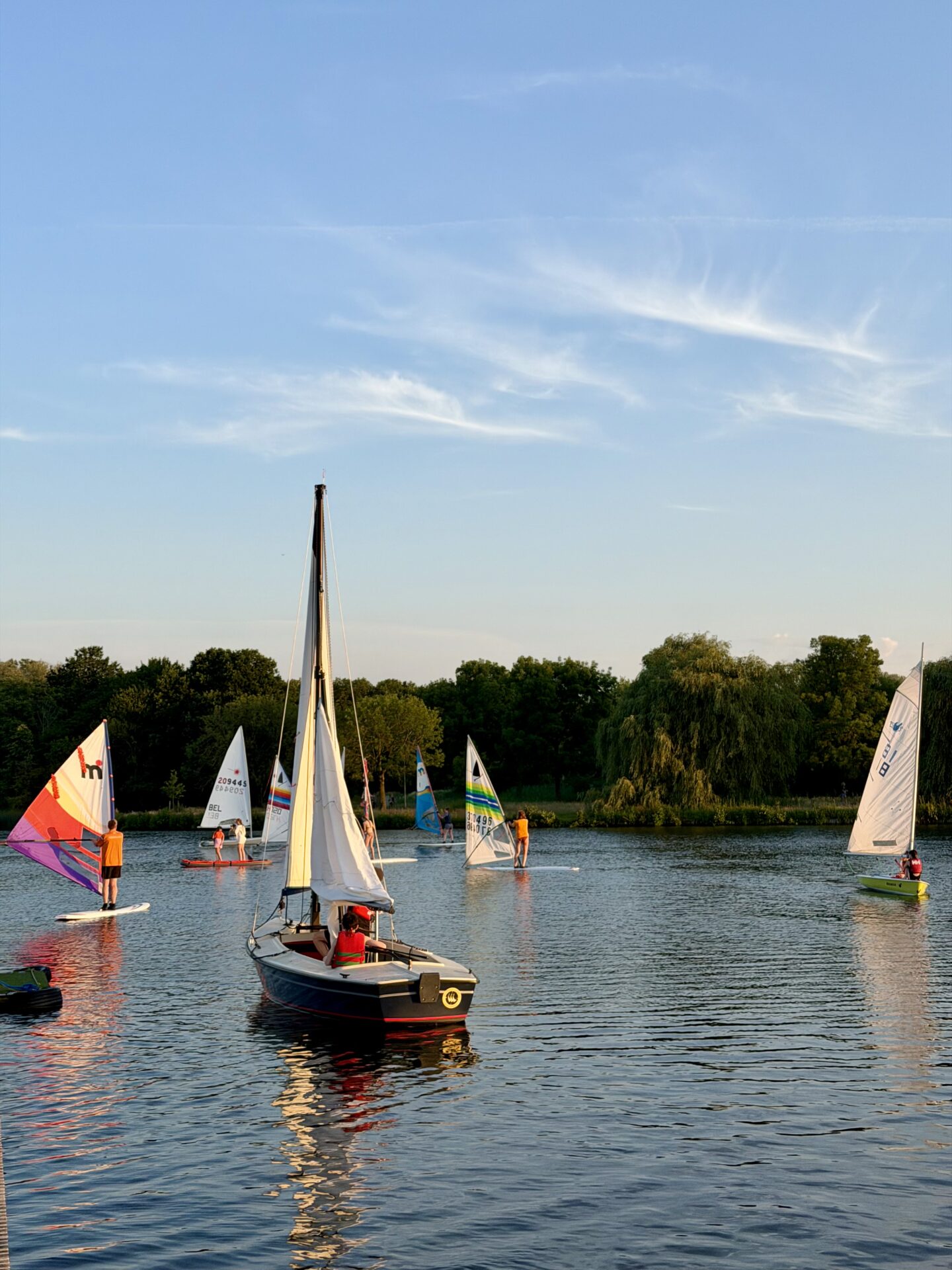 Een Valk zeilboot en windsurfers varen bij avondlicht op de Oosterplas tijdens Midzomernacht 2026.